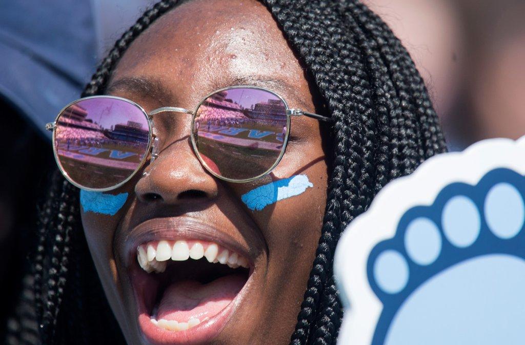 一位黑人女学生举着焦油跟形状的泡沫手指为美国欢呼.N.C. 足球队.