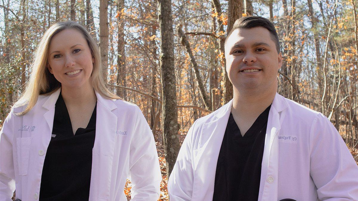 Cy and Kandis Fogleman wearing lab coats and black shirts in front of bare trees.