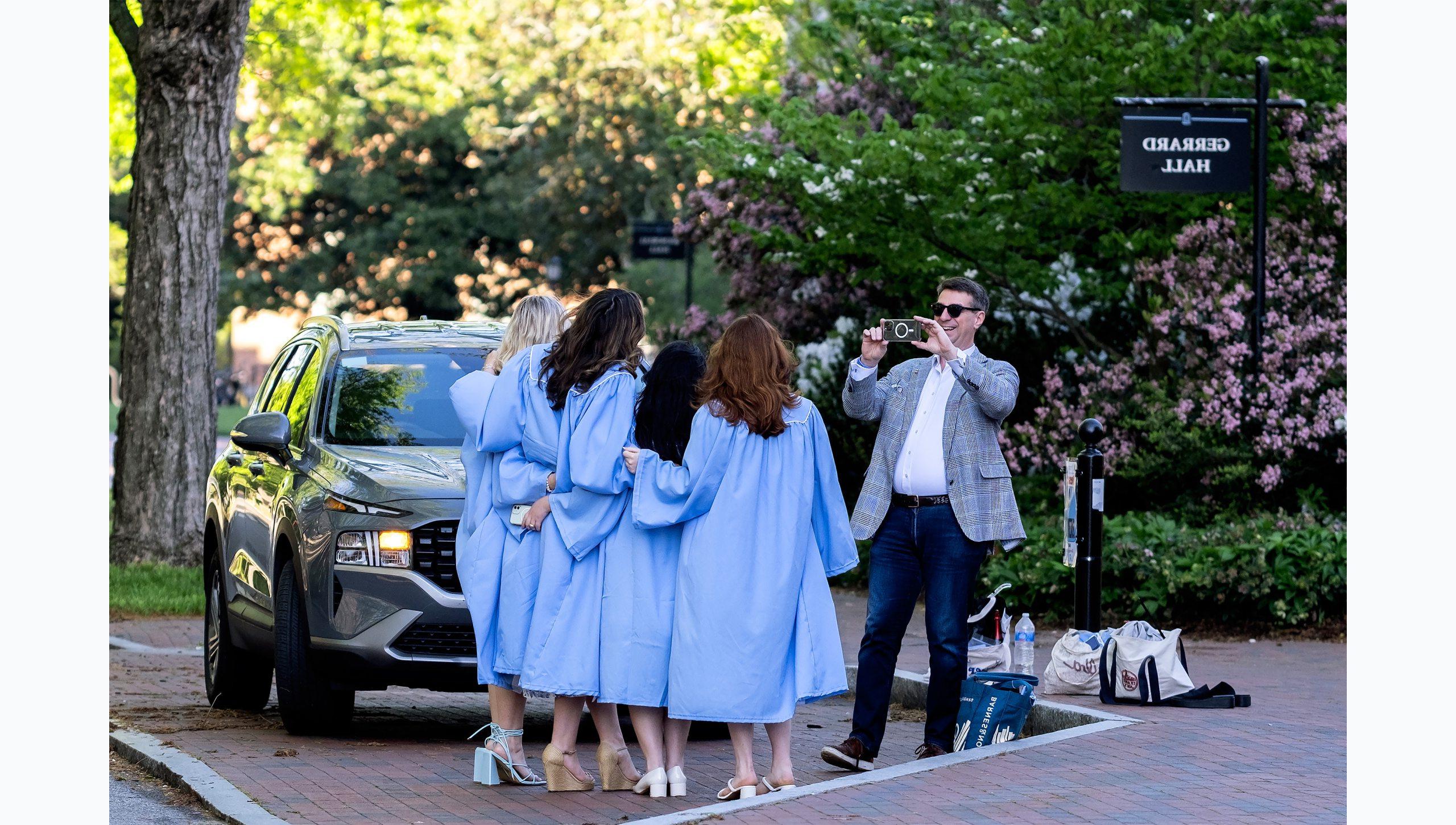 一名男子用手机给一群穿着毕业礼服的学生拍照.