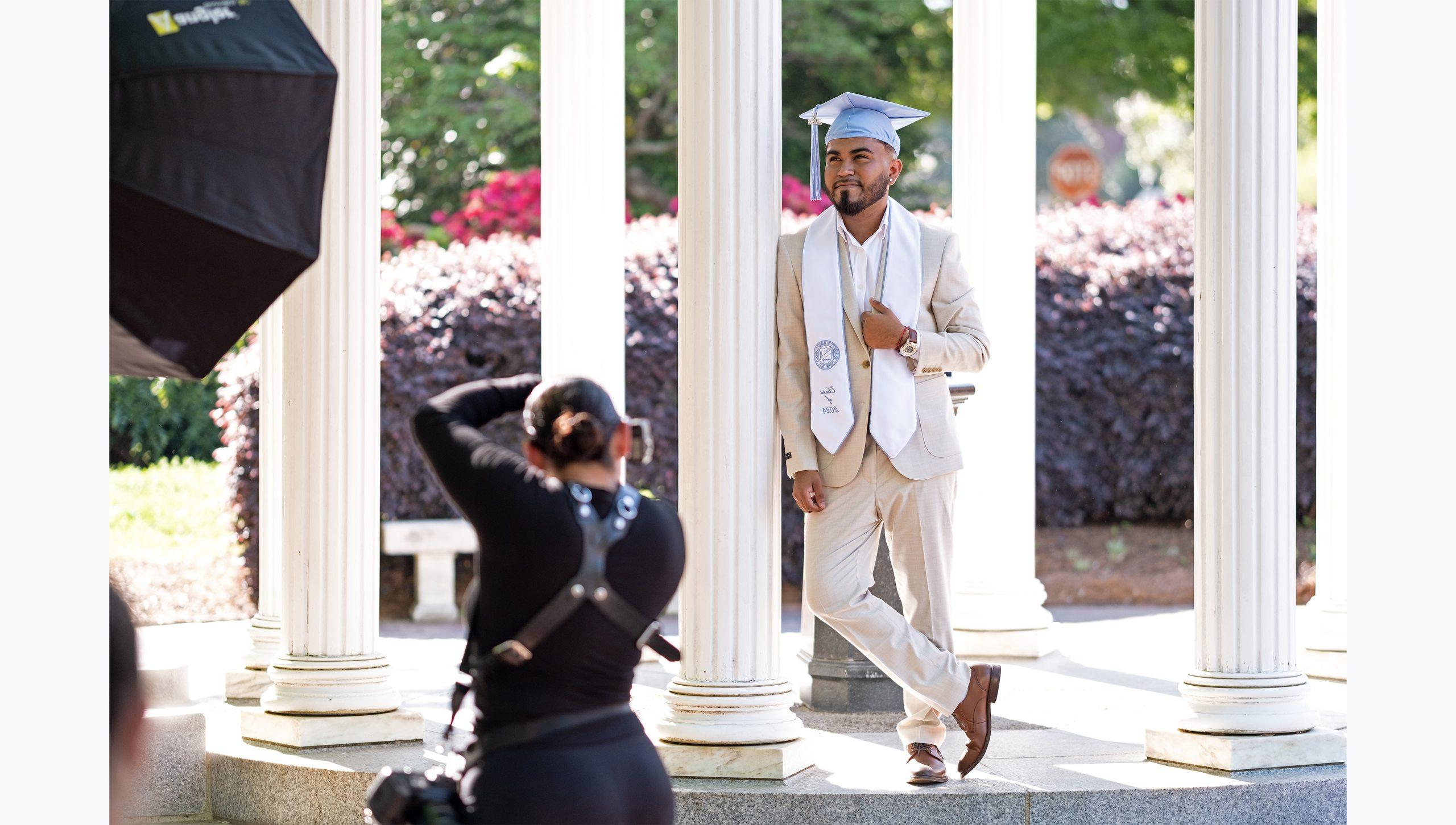 一名学生穿着西装，戴着毕业帽，在老井拍毕业照.