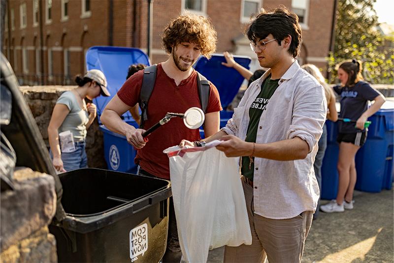两个学生，一个拿着垃圾袋，另一个在里面放了一个塑料盖子.