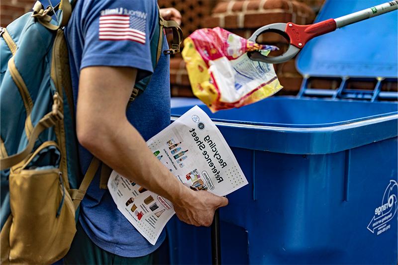 A student inspecting items inside a recycling bin