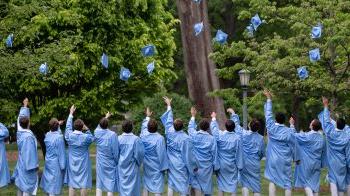 Group of students in graduation gowns throwing caps into the air
